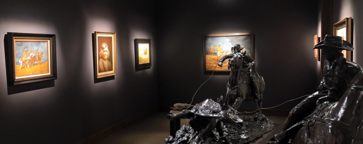 Cowboys gallery with precise spot lighting, bronze sculpture, and dark saturated walls